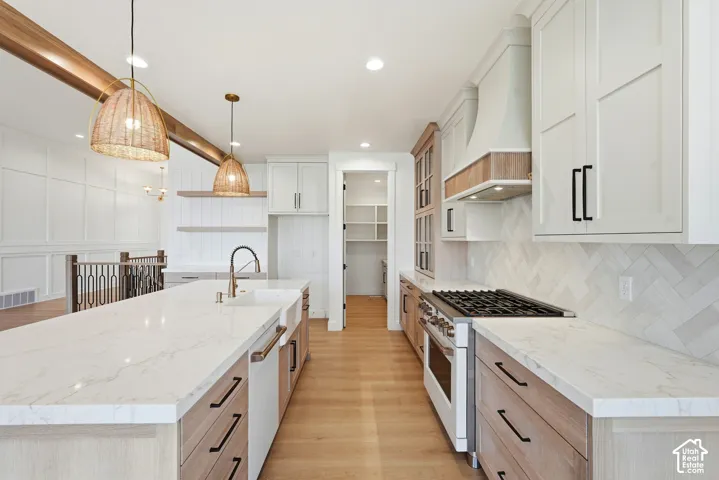 Spacious kitchen featuring an extended island with a built-in sink, stainless steel gas range, herringbone tile backsplash, and light wood-finish flooring