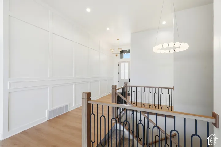 Wainscoting and paneled wall finishes, light wood-finish flooring, contemporary chandelier, recessed lighting, and a staircase with a wood handrail and black iron balusters