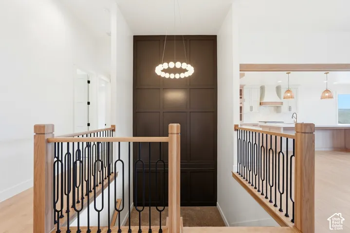 Natural wood handrails with black metal balusters, wood-finish flooring, accent wall with paneling, modern circular chandelier, and recessed lighting