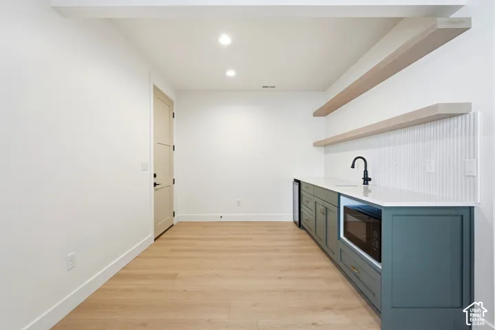 Modern wet bar with dark green cabinetry, white countertop, and light wood-finish flooring