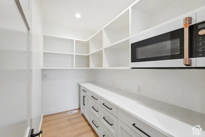 Built-in microwave, extensive shelving, white cabinetry with black hardware, light-toned wood-finish flooring, and recessed lighting