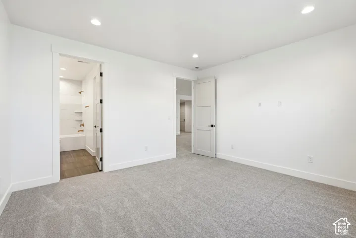 Recessed lighting illuminates a carpeted room with a full bathroom featuring a tub and shower combination with a tiled surround, recessed shelving, and wood-finish flooring