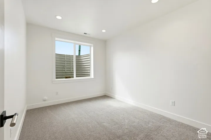Recessed lighting, light gray carpeting, white walls, white window trim, and a white door with a black and silver handle
