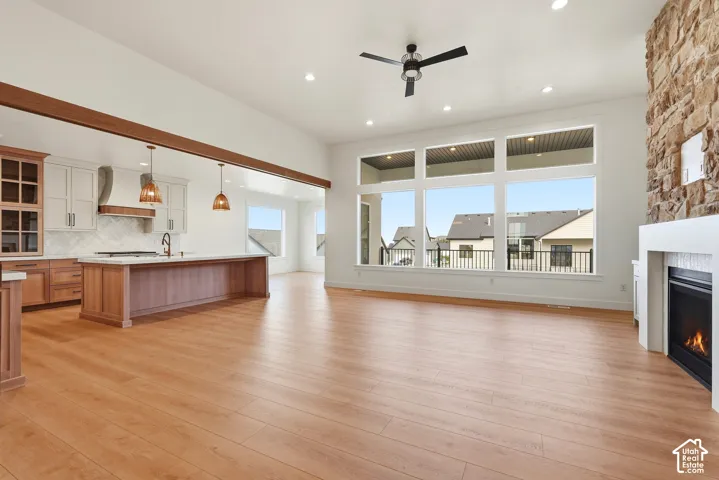 Expansive living area featuring wood-finish flooring, a stone-clad fireplace with a hearth, a ceiling fan, and large windows