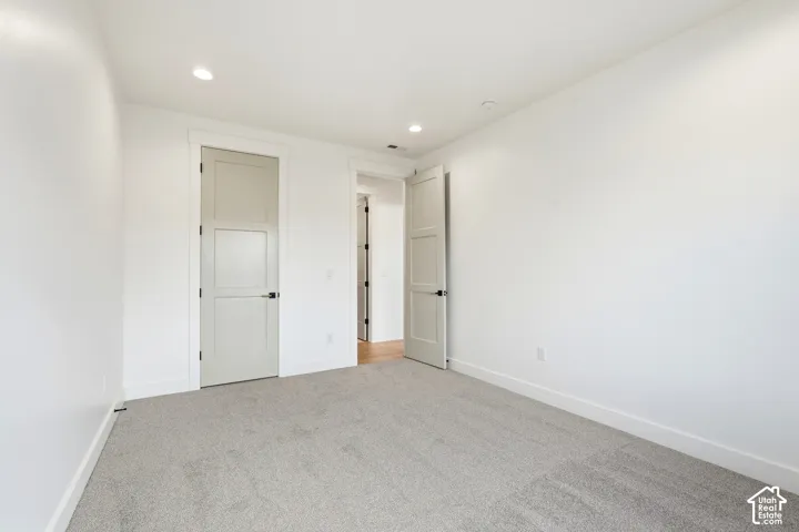 Recessed ceiling lighting, light gray paneled doors with black hardware, white walls, and light gray carpeting