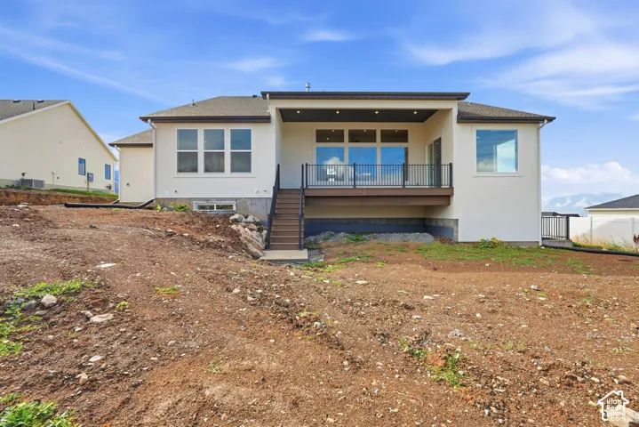 Rear stucco exterior featuring an elevated covered patio with recessed lighting, black railing, and stairs