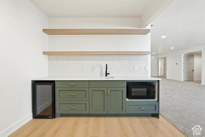 Built-in bar with green cabinetry, light-toned wood-finish flooring, quartz-finish countertop, and floating wood shelves