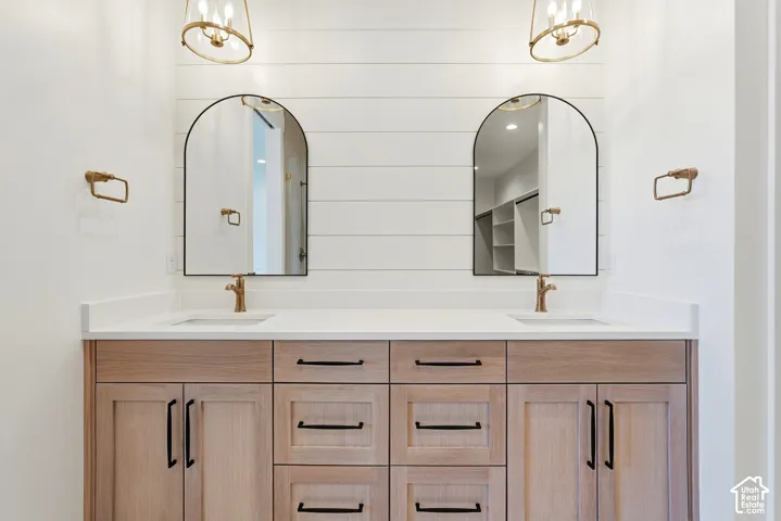Dual vanity with wood-finish cabinetry, white countertops, and arched mirrors
