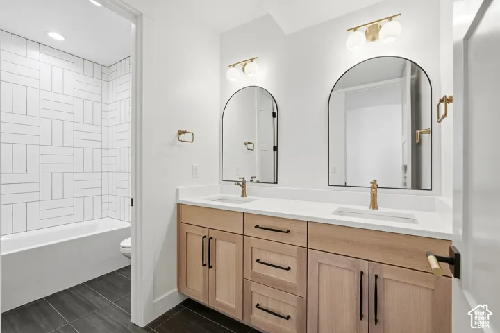 Double vanity with light wood-finish cabinetry, white countertops, and gold-tone fixtures
