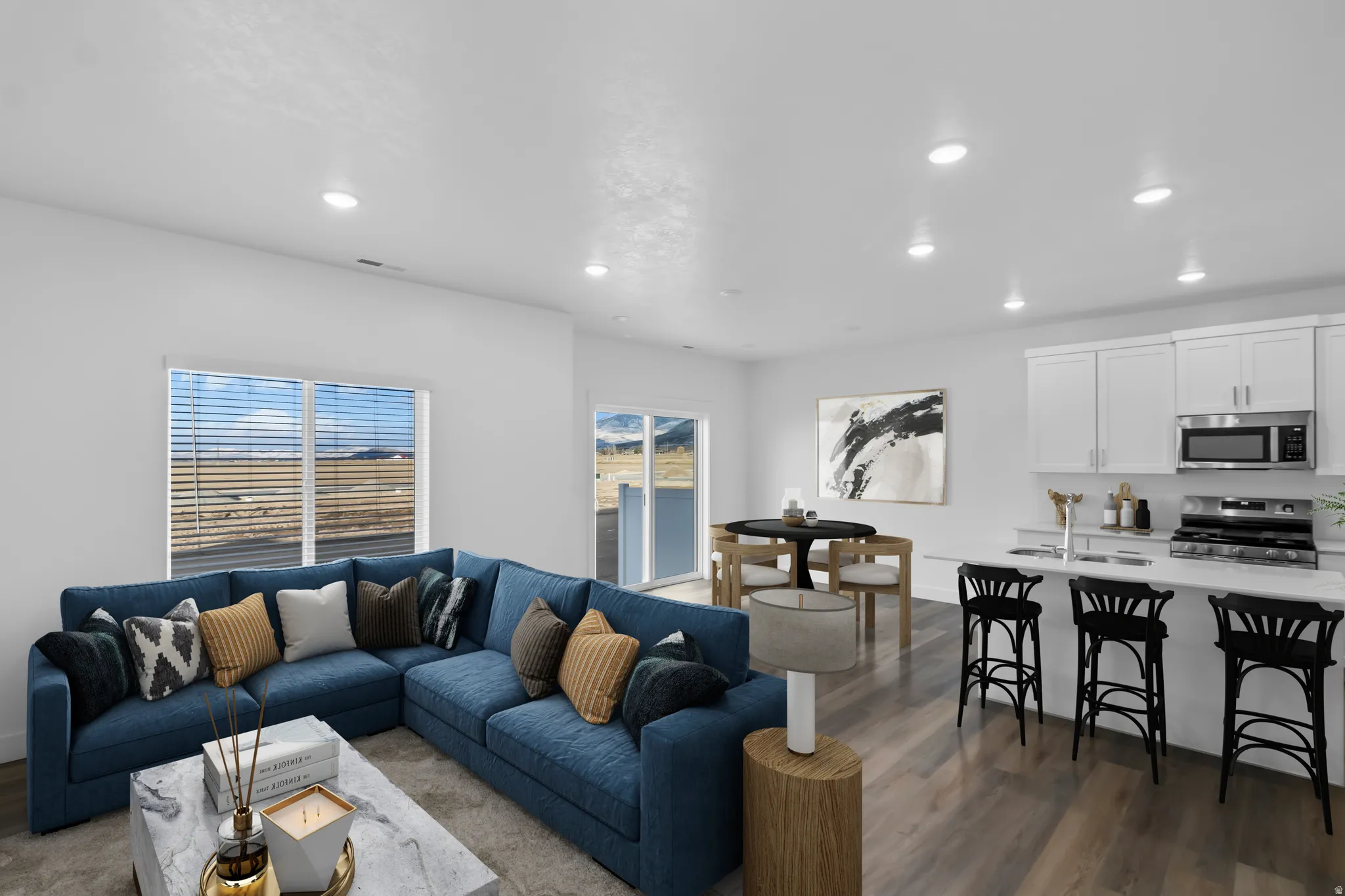 Open-concept living area featuring wood-finish flooring, recessed lighting, and a kitchen with white cabinetry and stainless steel appliances