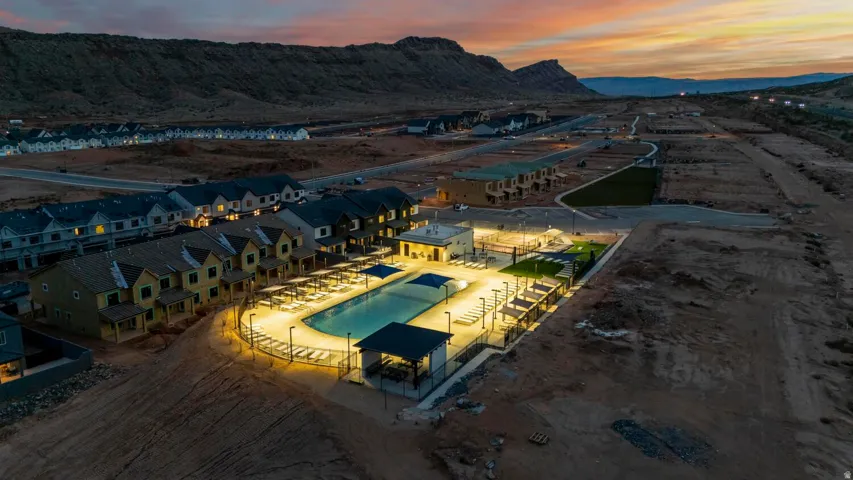 Community pool with integrated lighting, surrounding lounge areas, multiple shade structures, and an adjacent green space, all set against a mountain backdrop