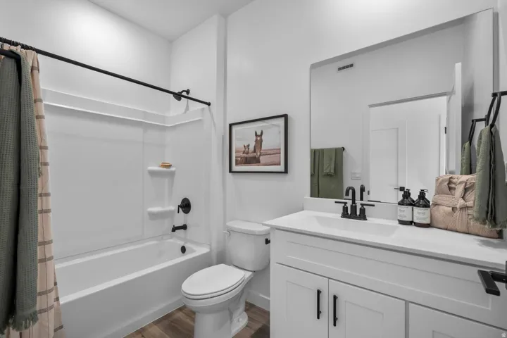 Clean-lined bathroom featuring a white vanity with integrated sink, matte black fixtures, a white bathtub with shower, and wood-finish flooring