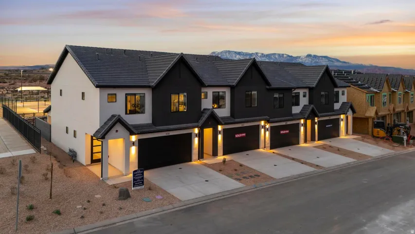 Modern townhome development featuring a black and white exterior facade, dark shingle roofs, integrated garages, and exterior wall lighting