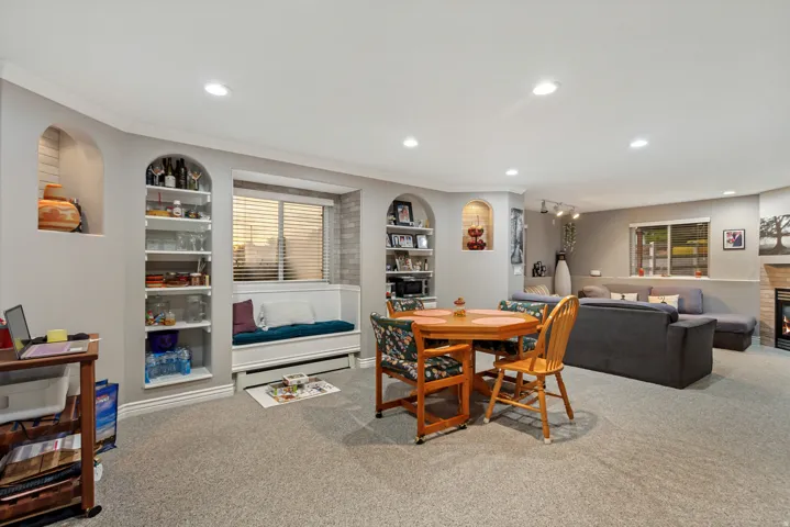 Carpeted recreation room featuring recessed lighting, built-in shelving, a window seat with storage, and a fireplace with a stone surround