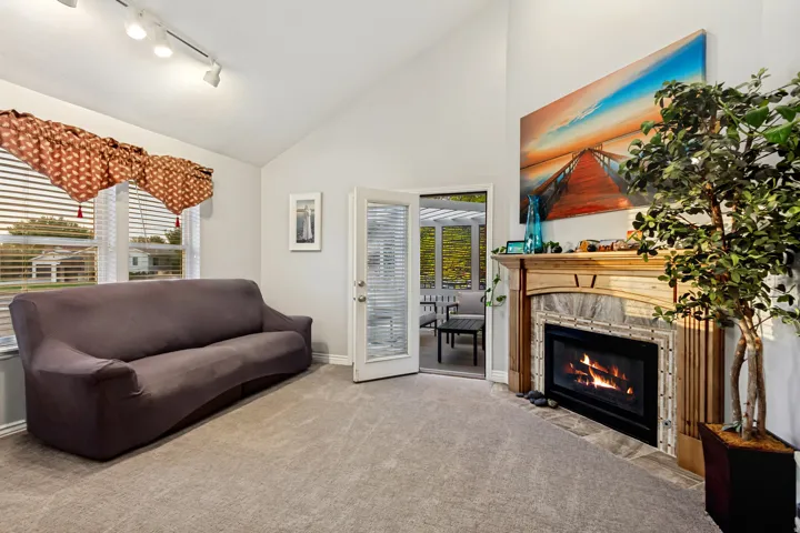 Vaulted ceiling, track lighting, wood-surround fireplace with stone tile, glass-paned French doors, and carpeted flooring