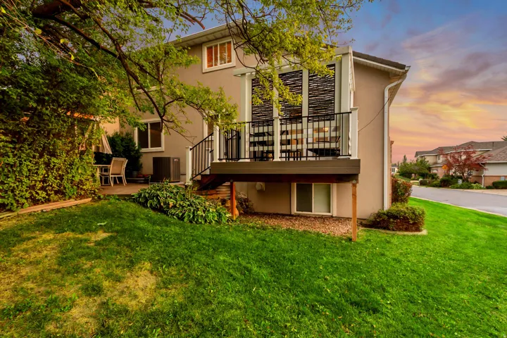 Raised deck with black metal railings, ground-level patio, mature landscaping, and stucco exterior