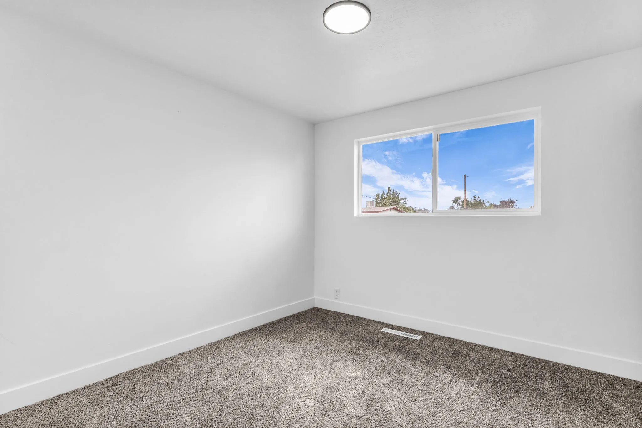 White walls, gray carpet, and a flush-mount ceiling light