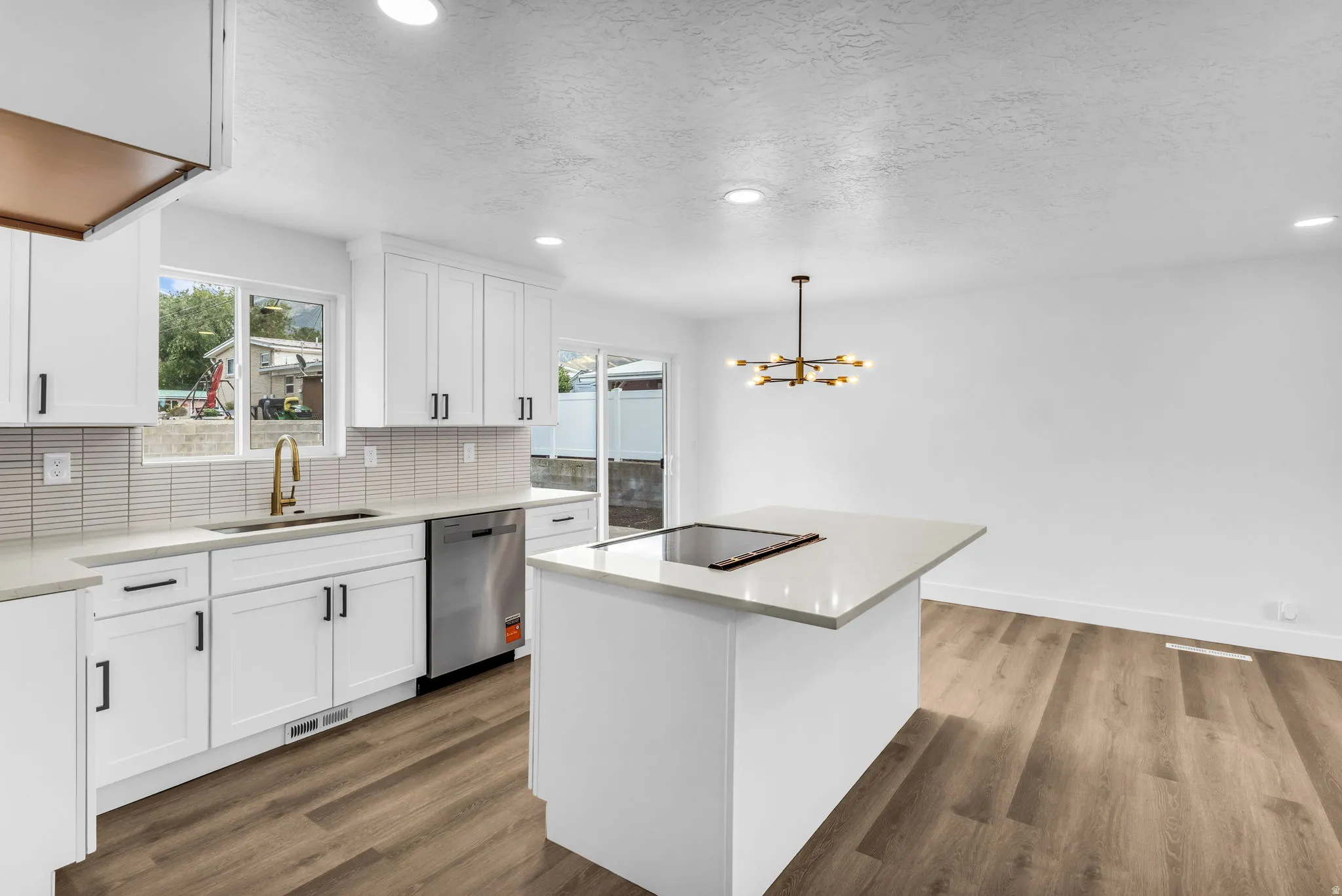 Modern kitchen featuring white shaker cabinetry, stainless steel dishwasher, wood-finish flooring, quartz countertops, and an island with an integrated cooktop