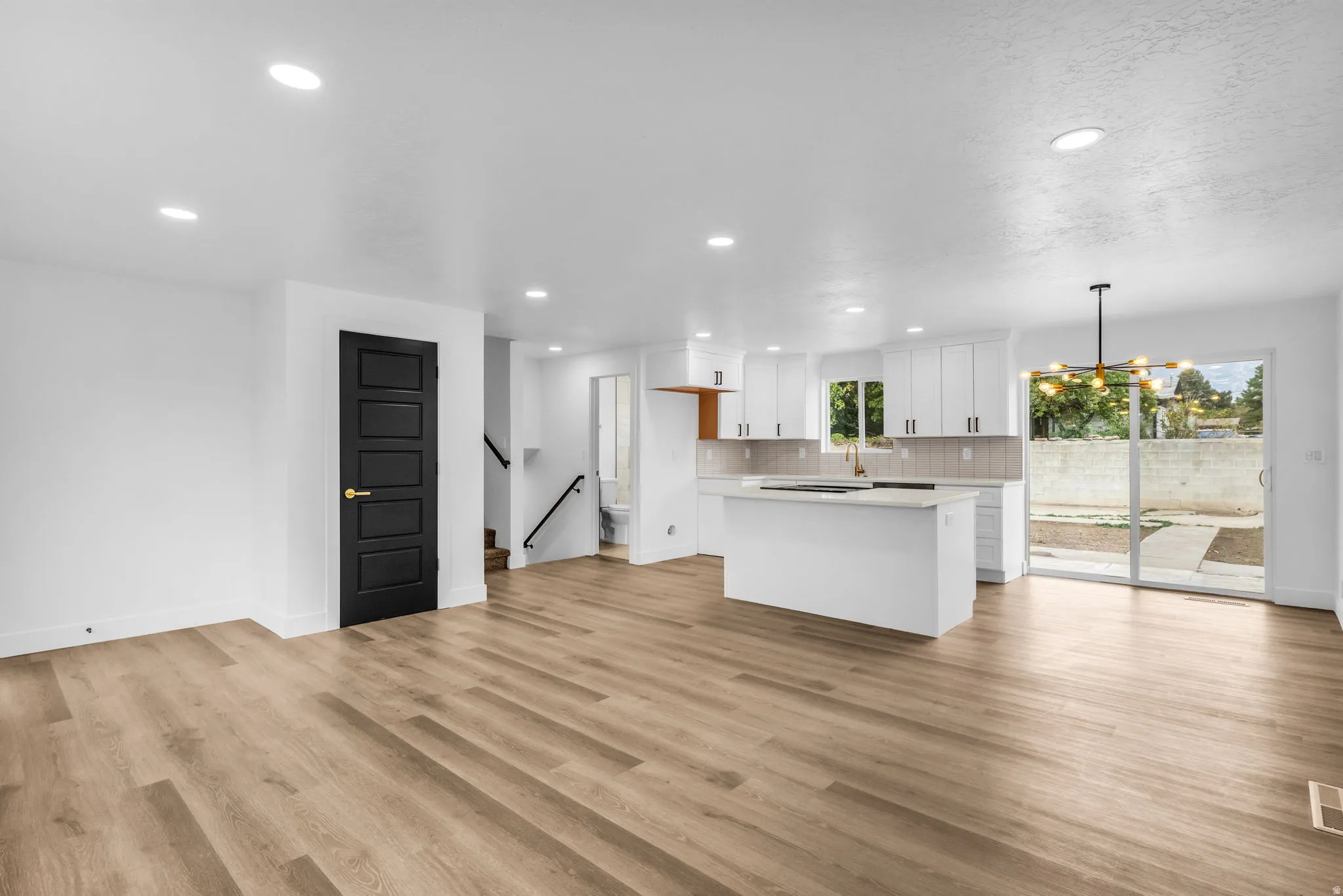Open-concept living space featuring wood-finish flooring, recessed lighting, and a kitchen with white cabinetry and a central island