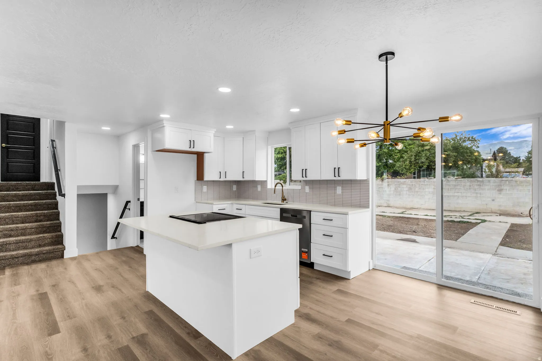 Modern kitchen featuring white cabinetry, a central island with a cooktop, wood-finish flooring, a contemporary chandelier, and sliding glass doors to the exterior