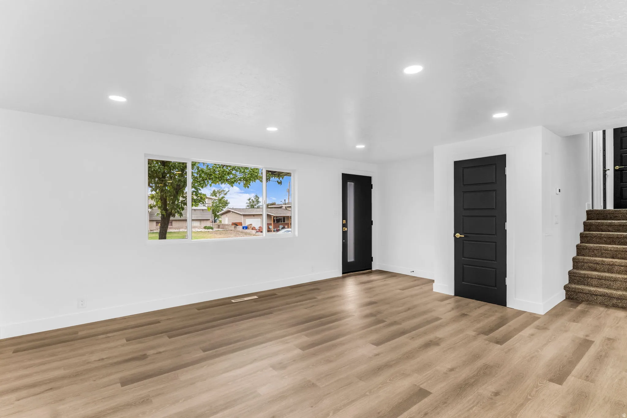 Wood-finish flooring throughout, recessed ceiling lighting, multi-pane window, and contemporary black doors with paneled detailing