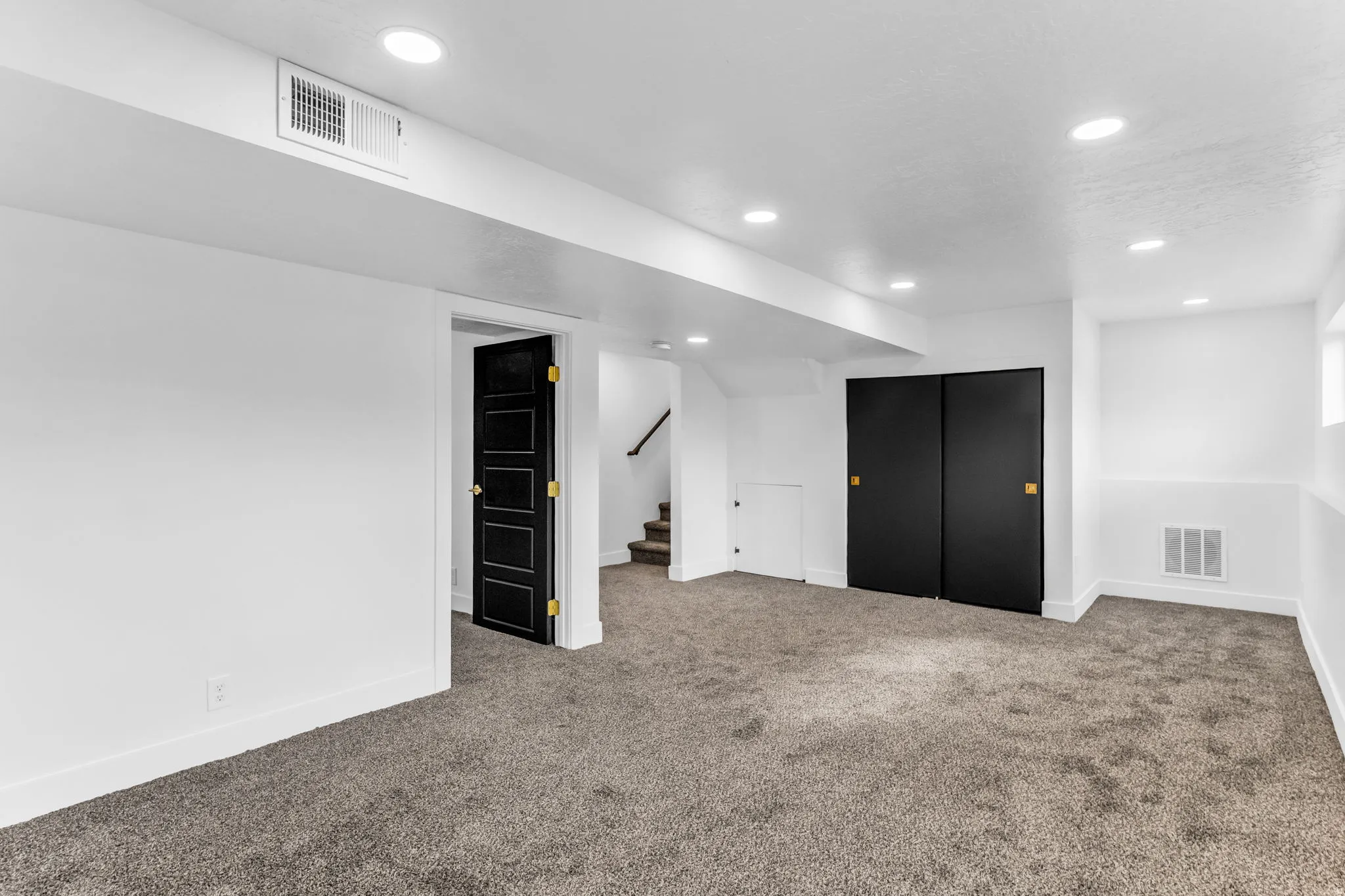 Expansive room featuring recessed lighting, plush carpeting, black panel doors, and contrasting white walls