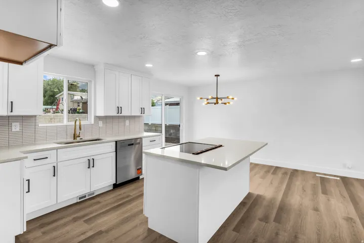 Modern kitchen featuring white shaker cabinetry, stainless steel dishwasher, wood-finish flooring, quartz countertops, and an island with an integrated cooktop