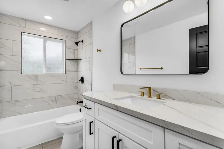White vanity with a light-toned countertop, gold-finish faucet, and a rectangular mirror