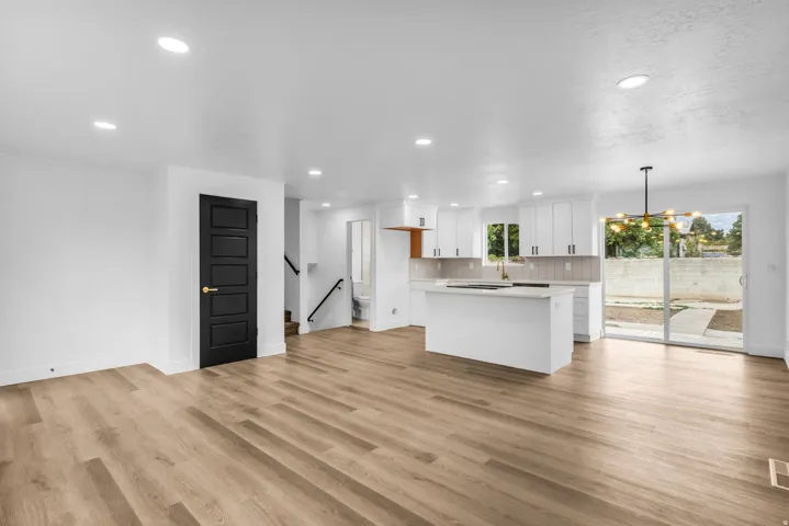 Open-concept living space featuring wood-finish flooring, recessed lighting, and a kitchen with white cabinetry and a central island