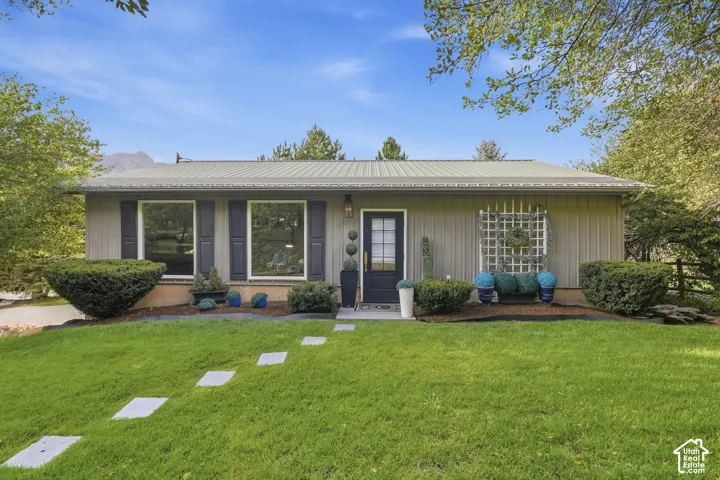 Single-story residence featuring a metal roof, front entry door with transom window, large picture windows with shutters, and a decorative trellis accent