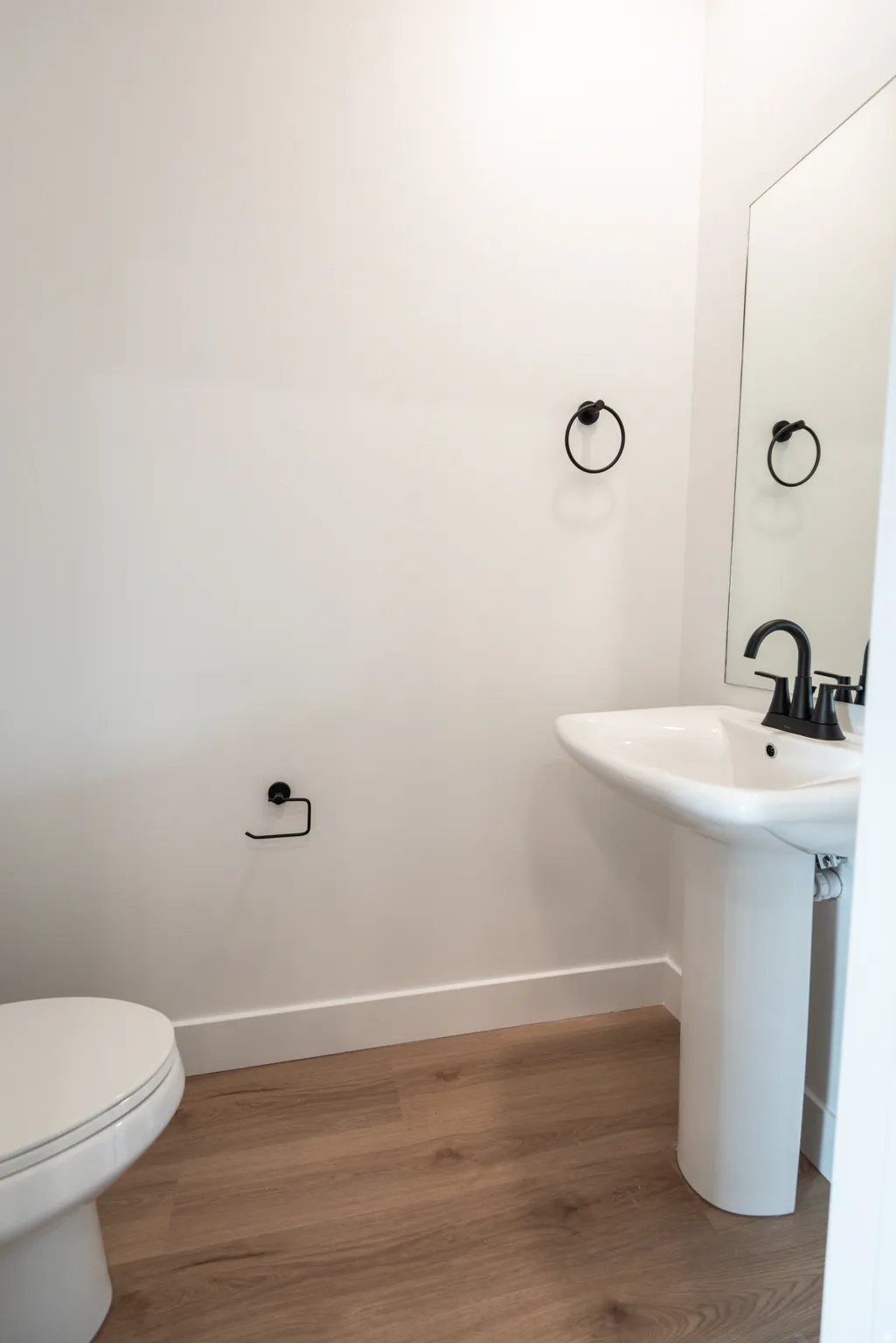 Pedestal sink with black faucet, wood-finish flooring, and white walls