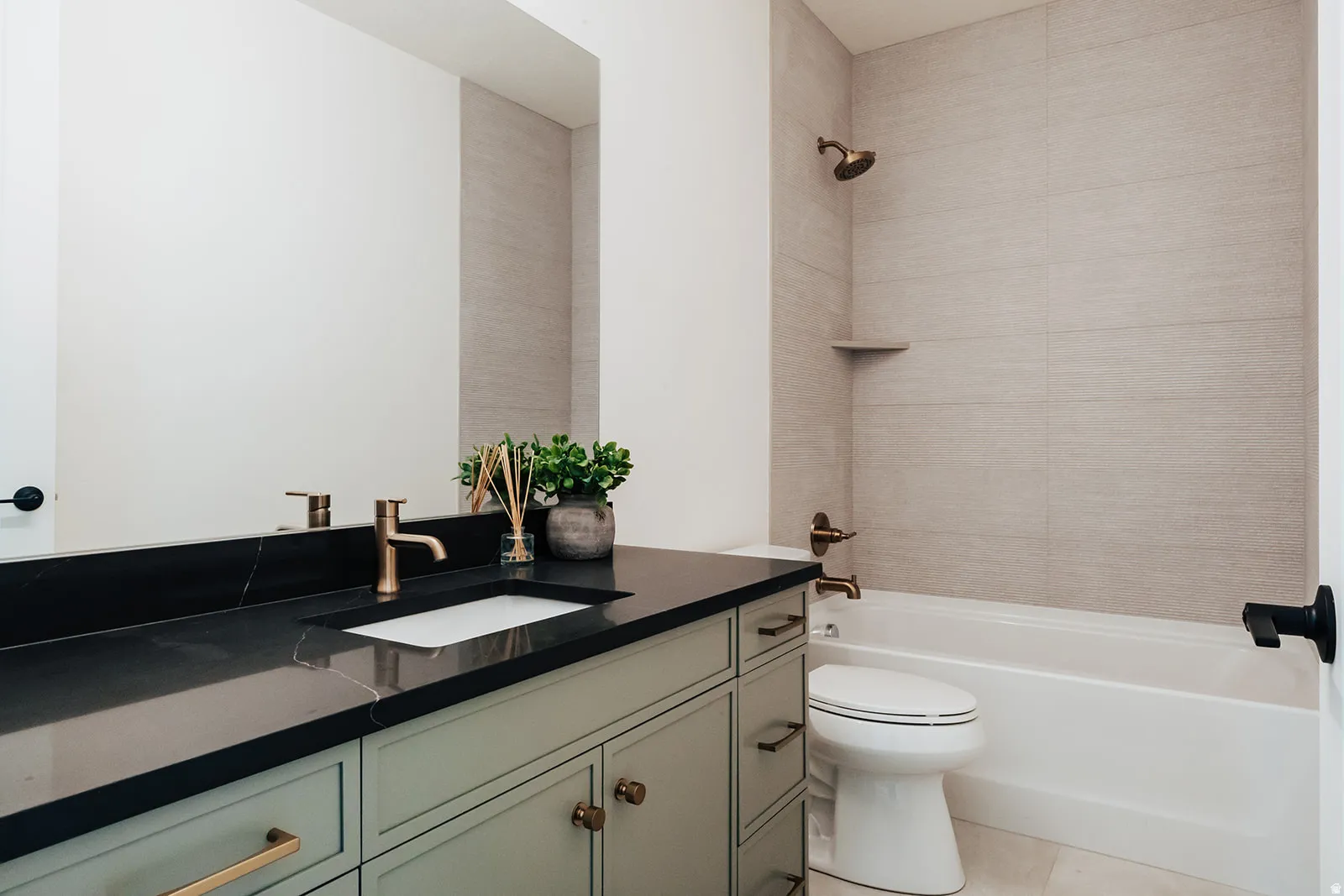 Sleek dark countertop with an integrated rectangular sink, light green cabinetry, and brushed brass hardware