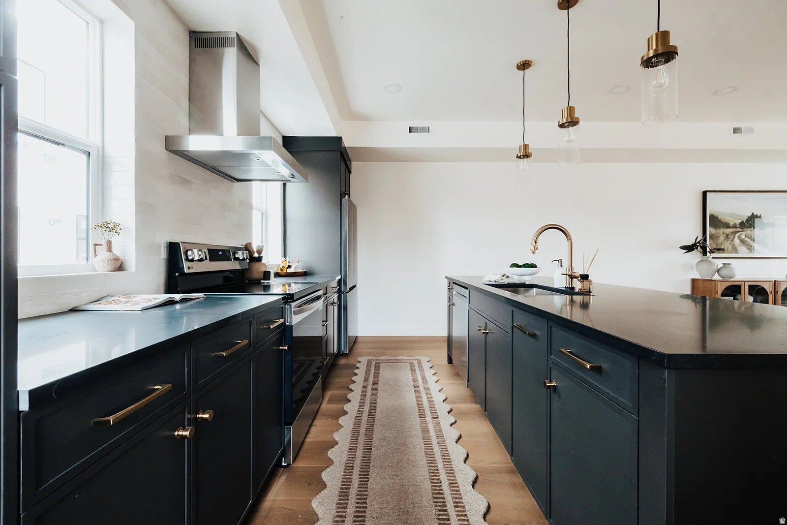 Kitchen featuring dark cabinetry, light wood-finish flooring, a stainless steel range hood, an undermount sink with a brass-finish faucet, and pendant lighting