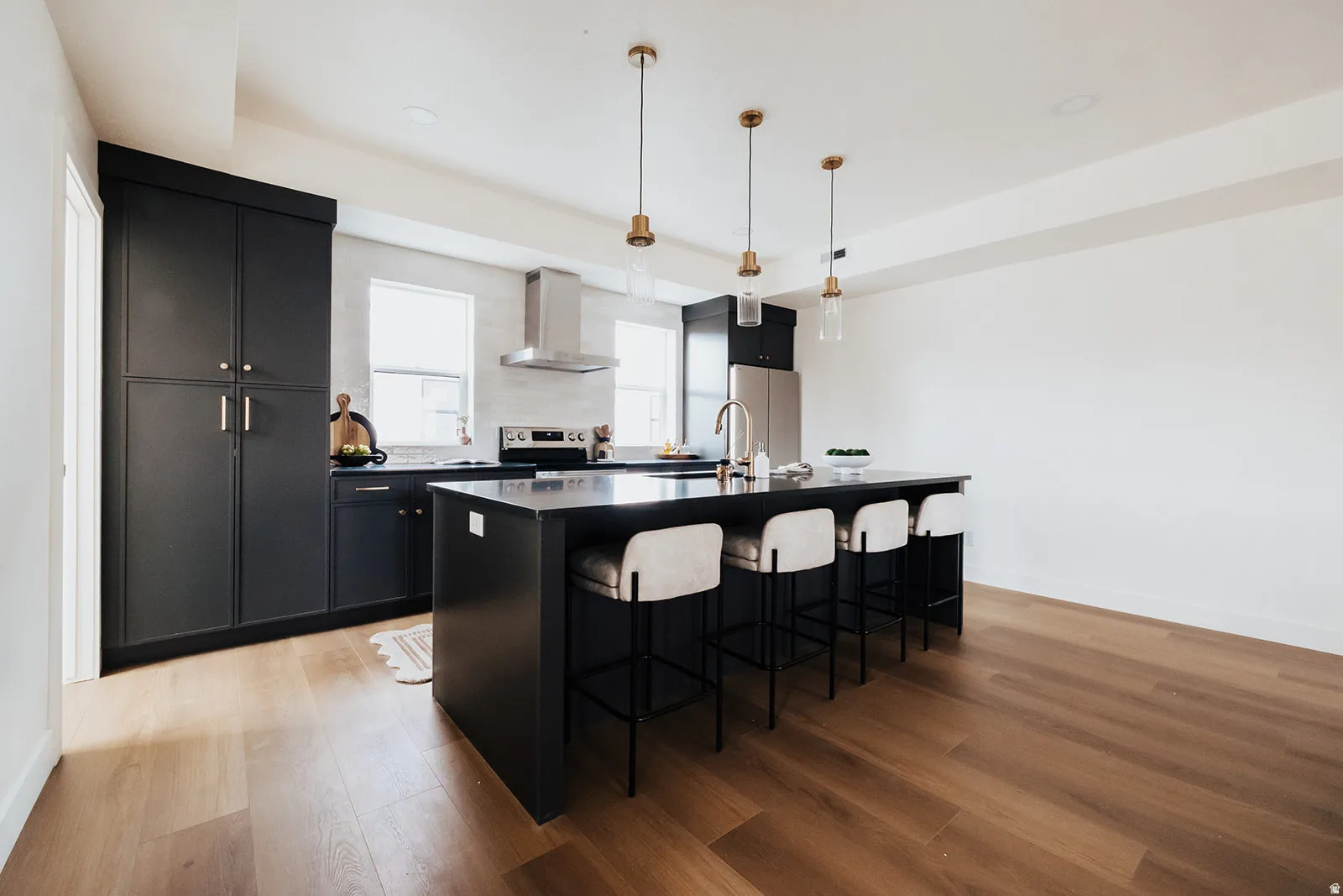 Modern kitchen featuring dark cabinetry, stainless steel appliances, a center island with seating, pendant lighting, and wood-finish flooring