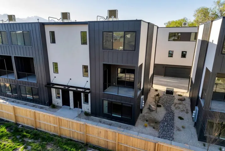 Modern townhome exterior featuring vertical metal siding, white stucco, and stone veneer accents