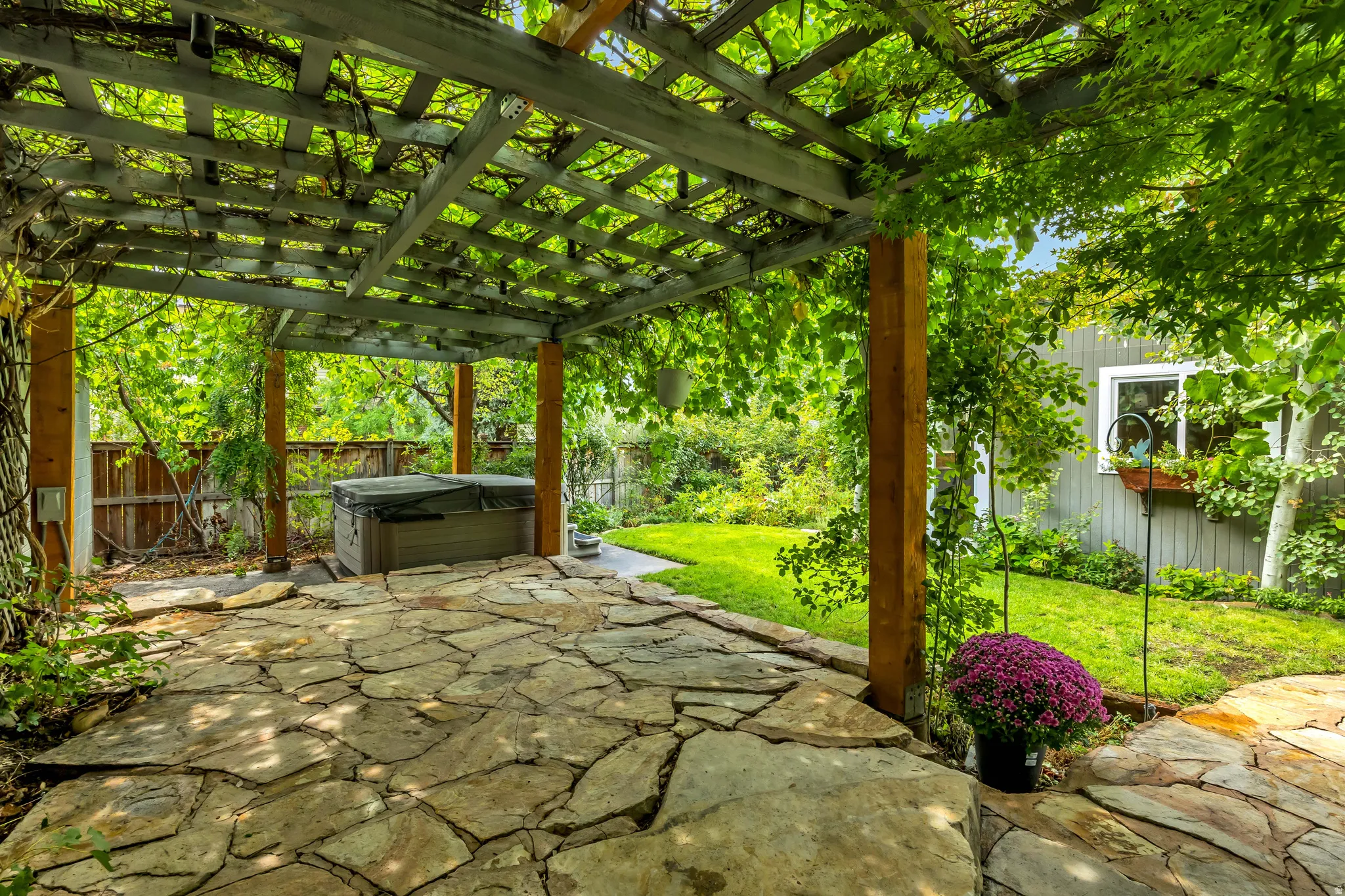 Wood pergola with lush overhead foliage, flagstone patio, built-in spa, and established lawn
