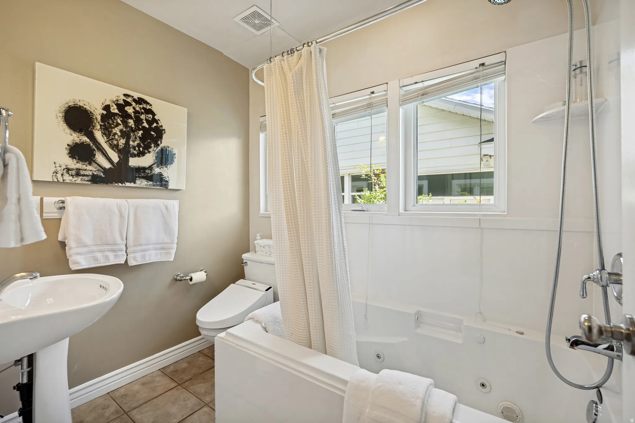 Pedestal sink, wall-mounted faucet, jetted tub, tiled flooring, and dual windows