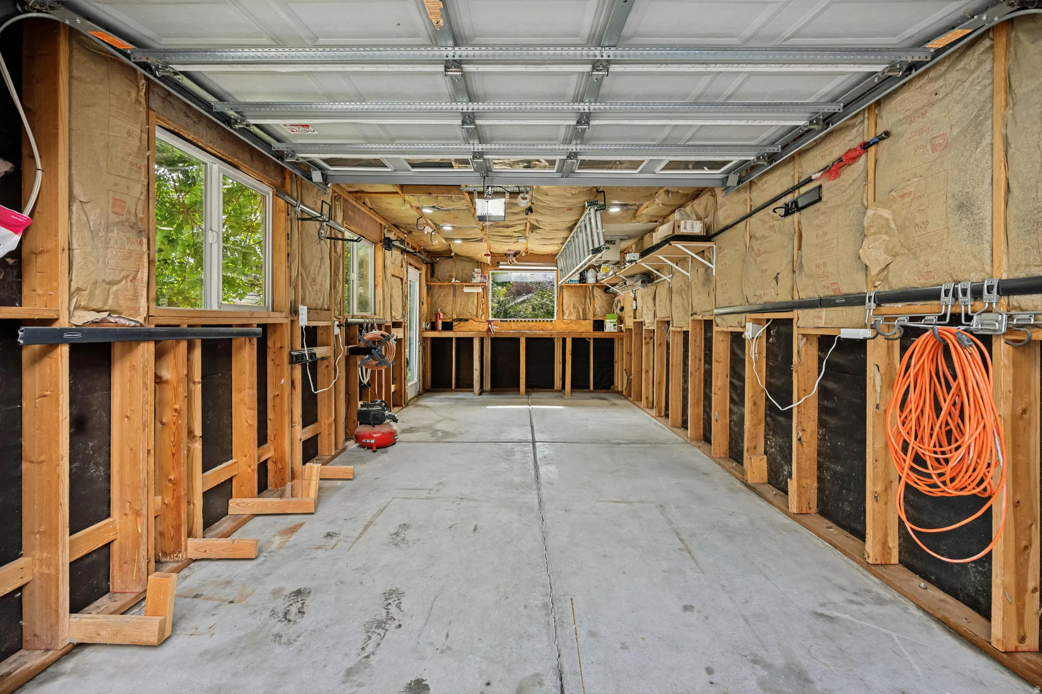 Lots of natural light in garage featuring exposed framing, multiple windows, built-in shelving, workbench and a concrete floor
