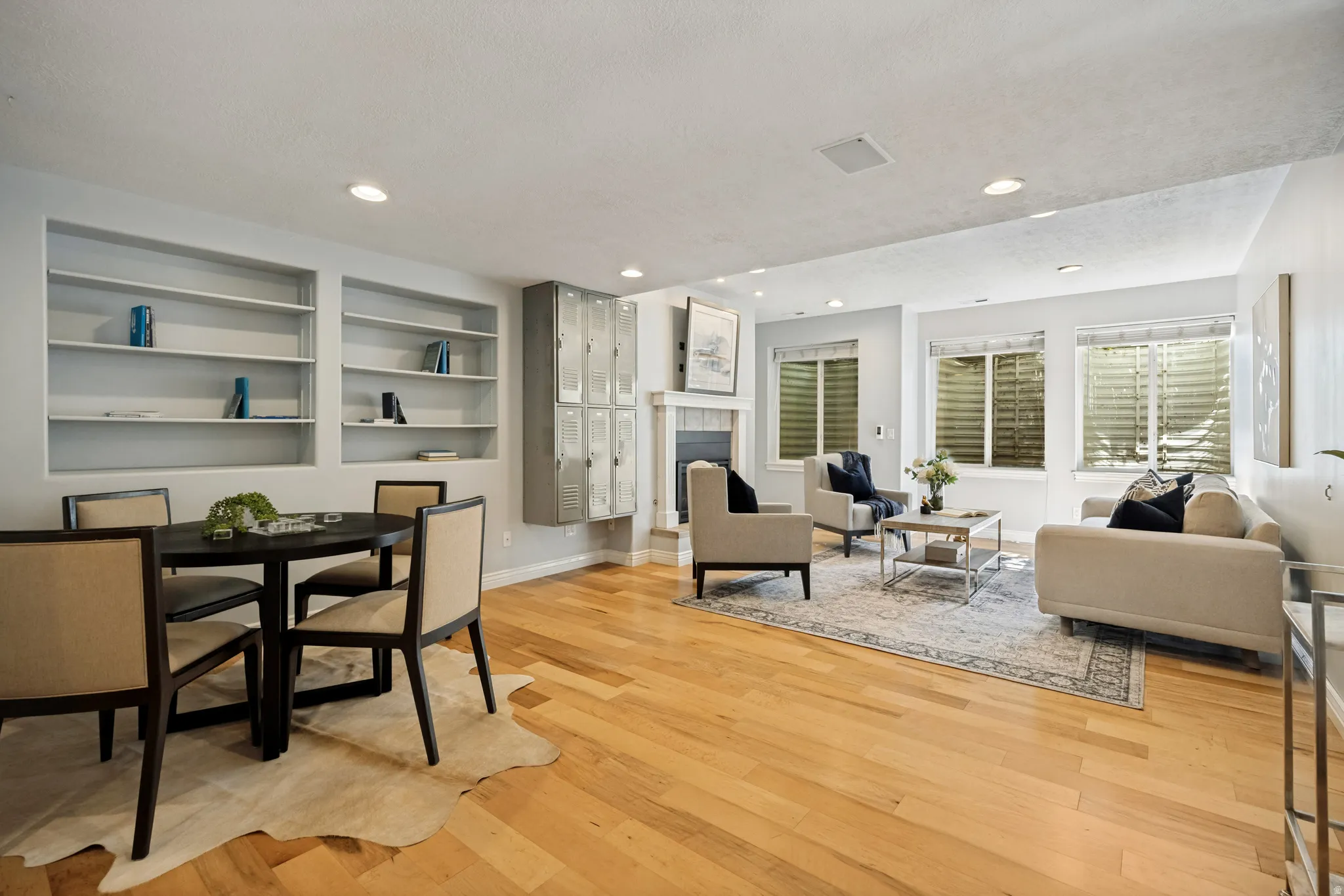 Light wood-finish flooring throughout, recessed lighting, built-in shelving, fireplace, and multiple windows with blinds