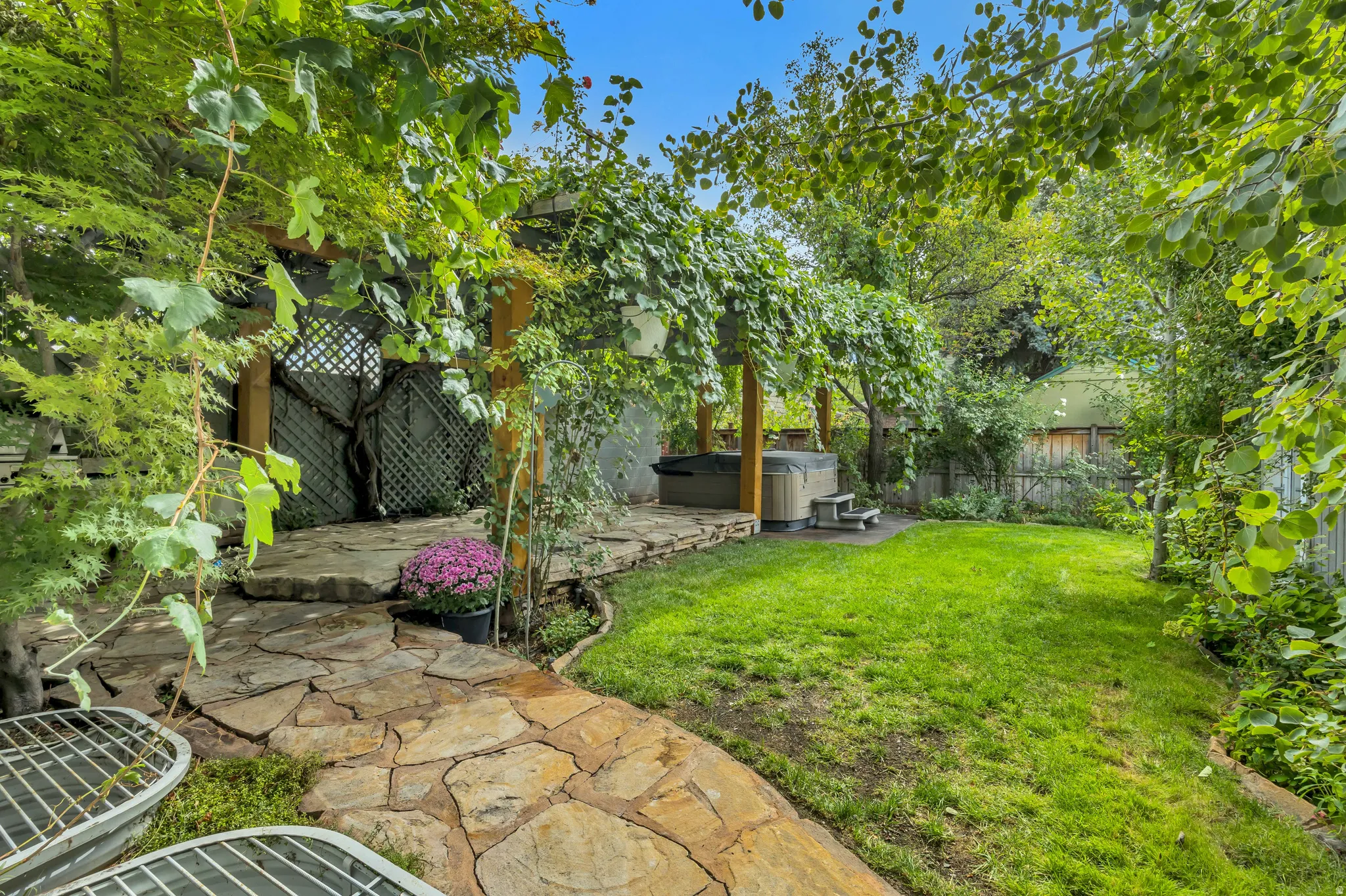 Manicured lawn with flagstone pathways, a wood-framed pergola, and an integrated hot tub feature