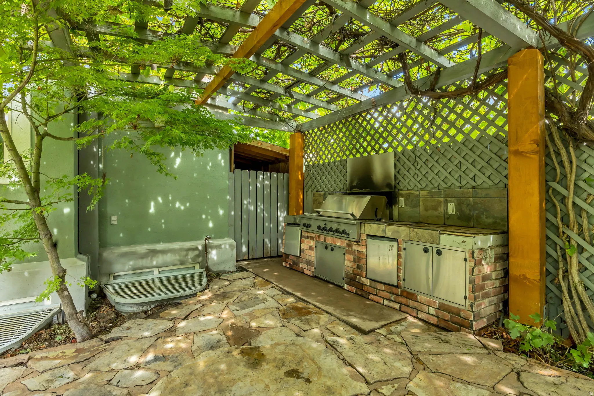 Outdoor kitchen with a built-in grill, brick base, stainless steel cabinetry, and stone countertop