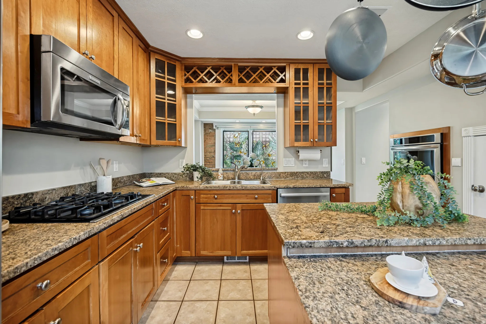 Kitchen featuring wood cabinetry, granite countertops, stainless steel appliances, tile flooring, and a pass-through window