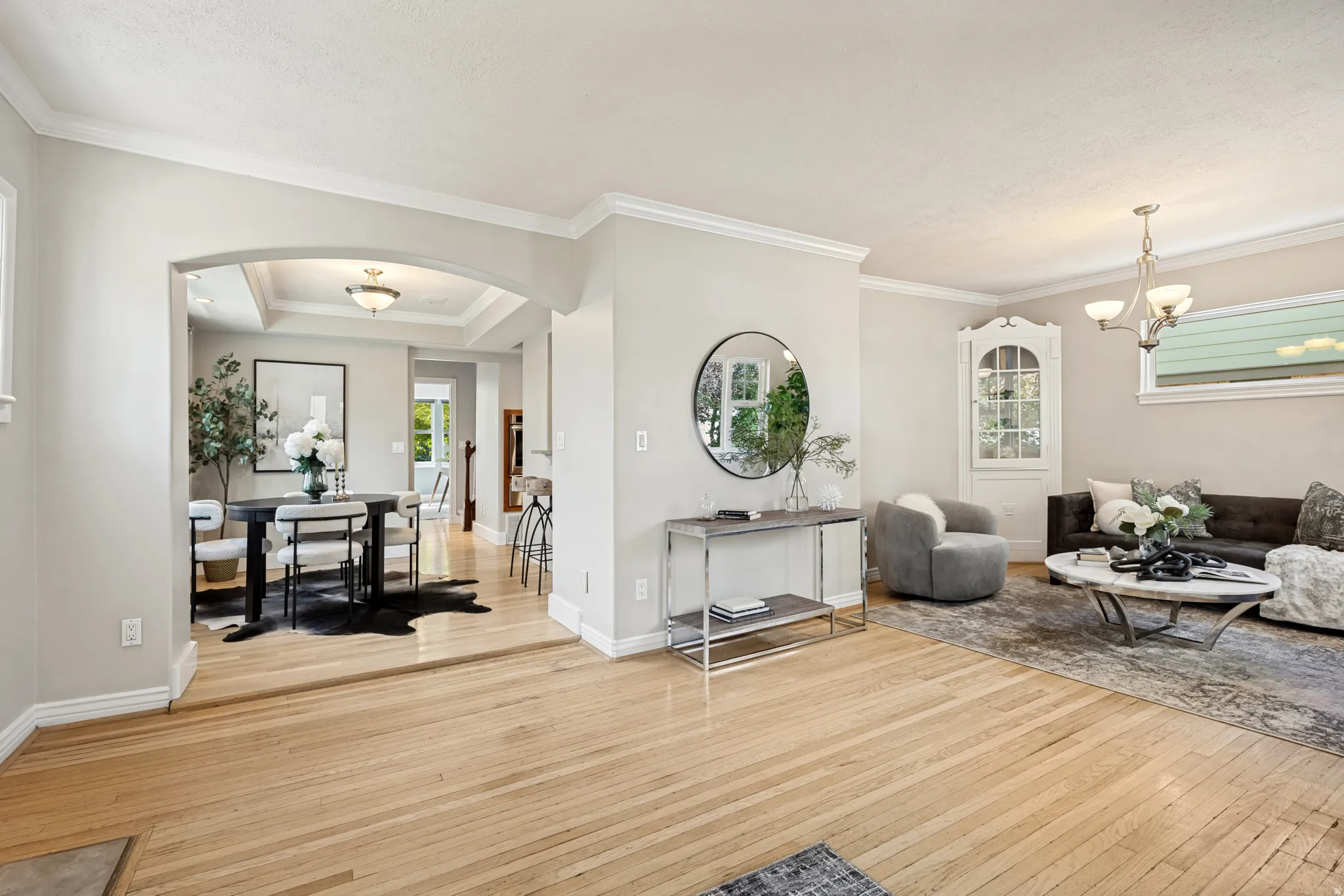 Hardwood flooring throughout, crown molding, arched entryway, tray ceiling, and built-in corner cabinet