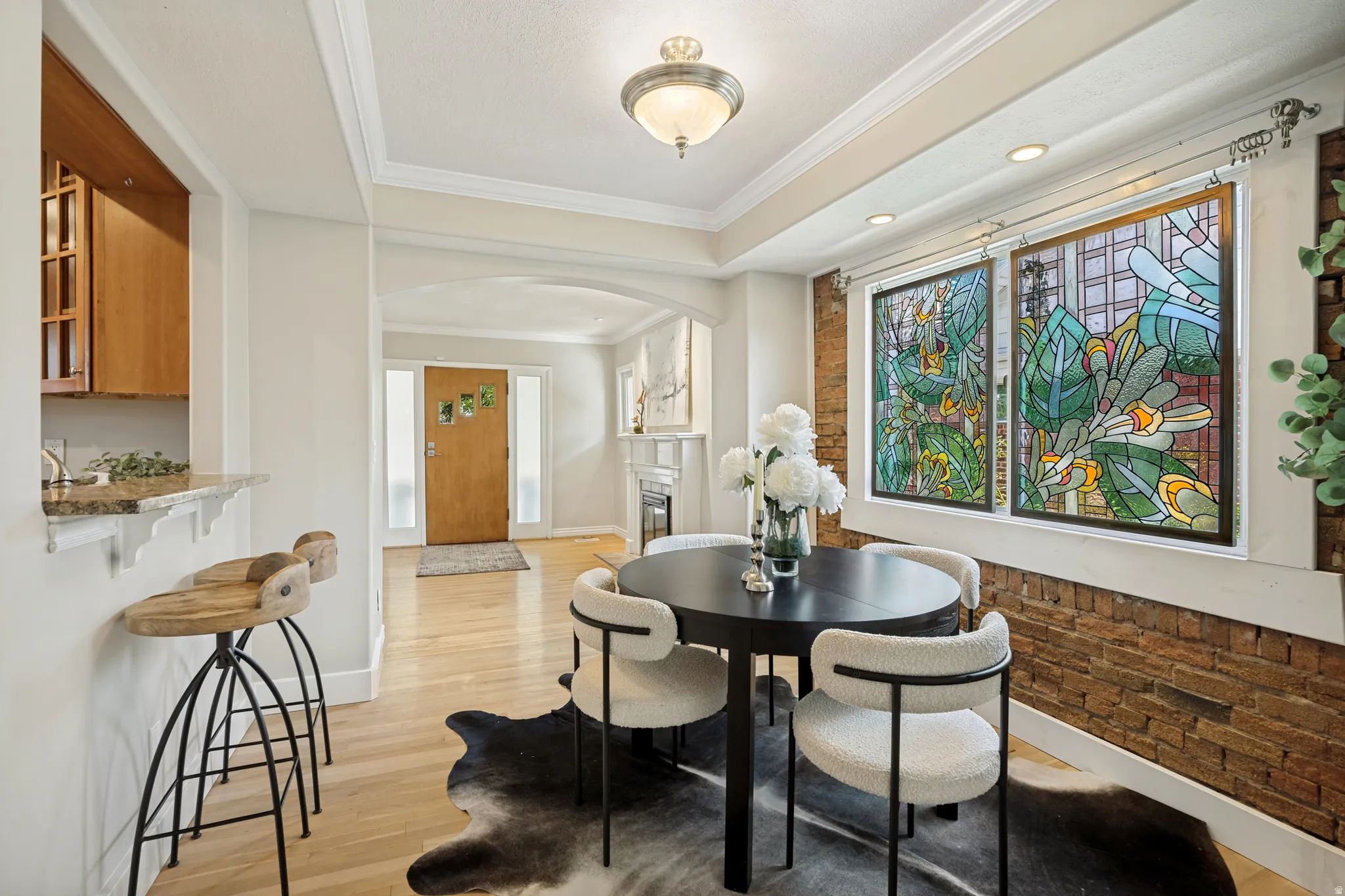 Hardwood flooring, crown molding, tray ceiling, exposed brick accent wall, and decorative stained glass panels