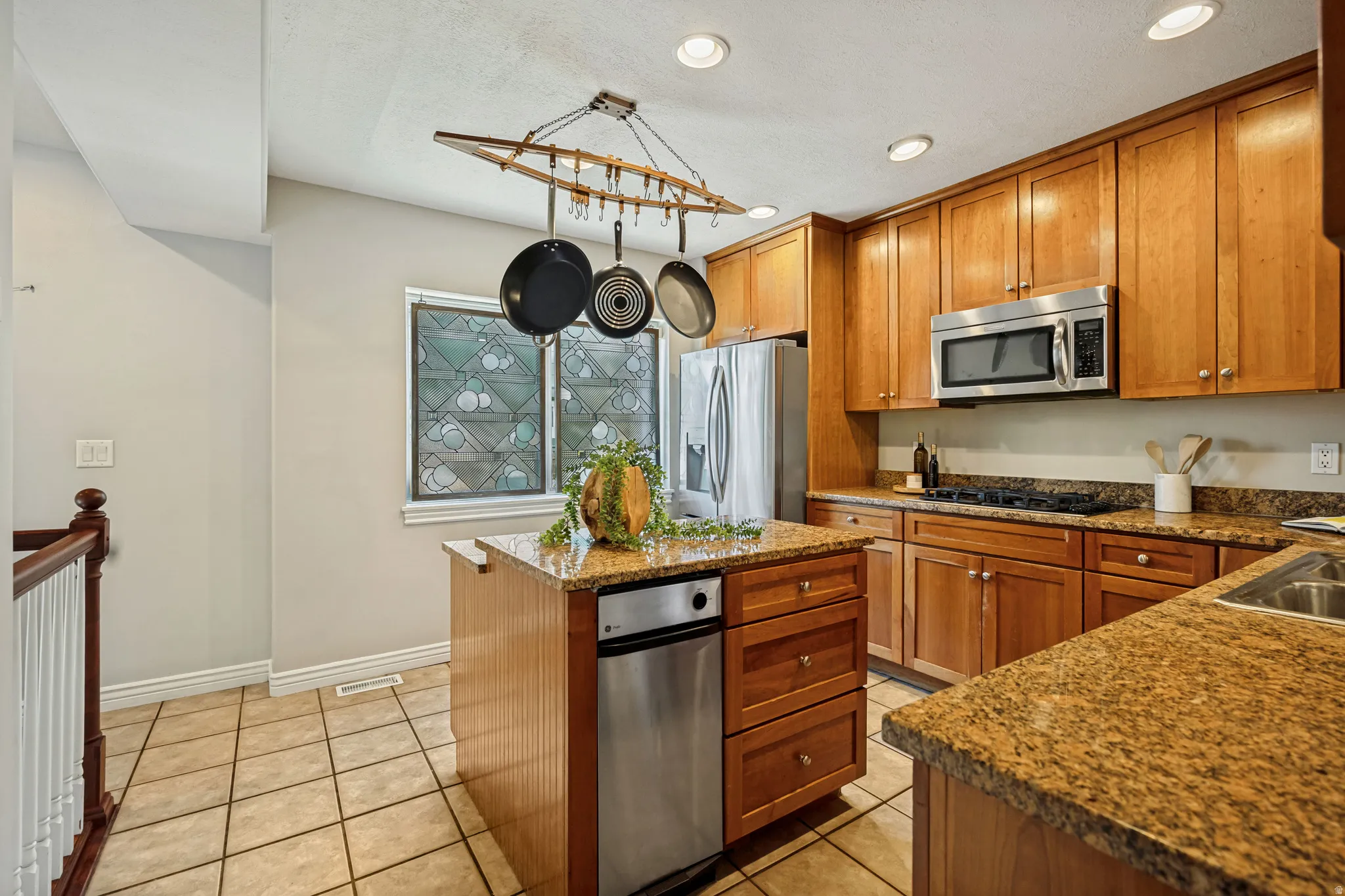 Kitchen featuring wood cabinetry, stainless steel appliances, a center island with a built-in dishwasher, and granite countertops