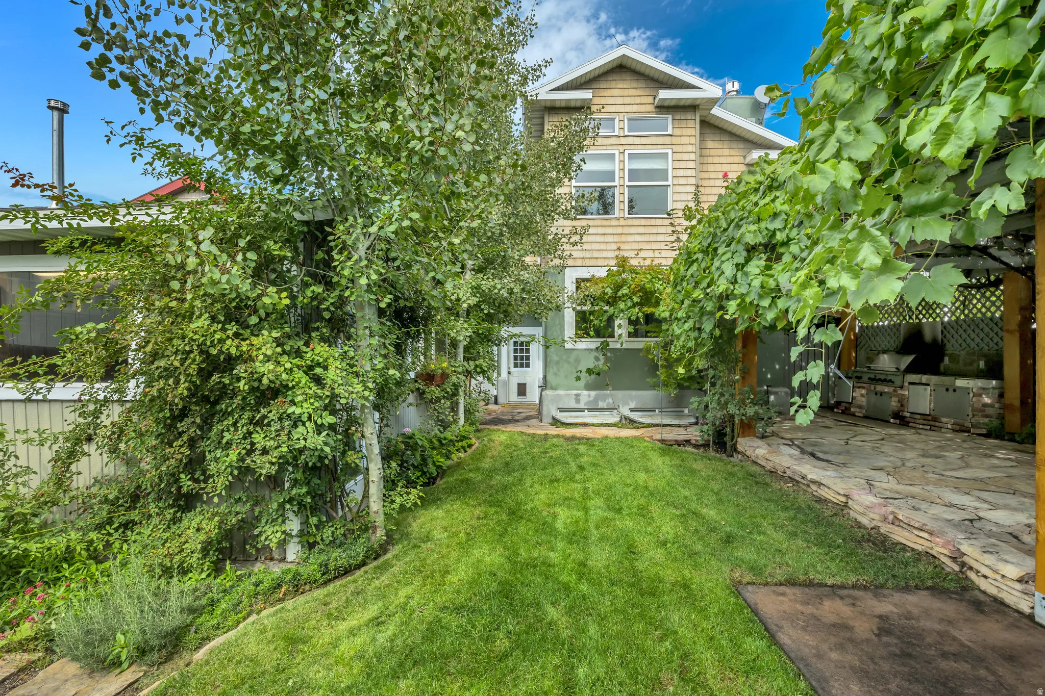 Expansive backyard featuring a manicured lawn, stone-paved patio, and mature landscaping
