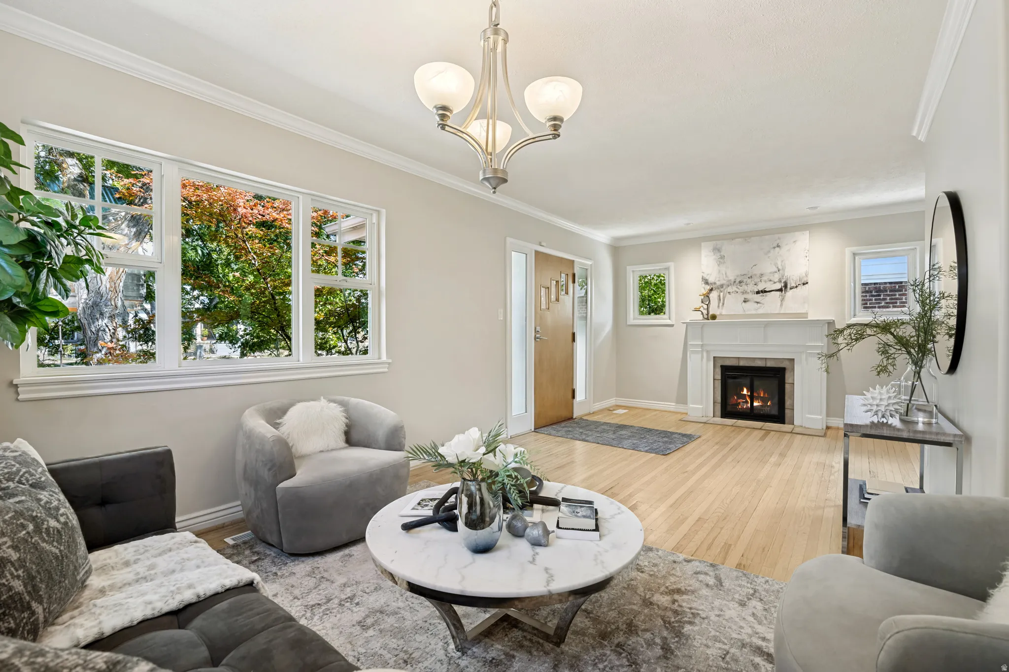 Hardwood flooring, white window trim, a traditional fireplace with a white mantel, crown molding, and a three-light chandelier