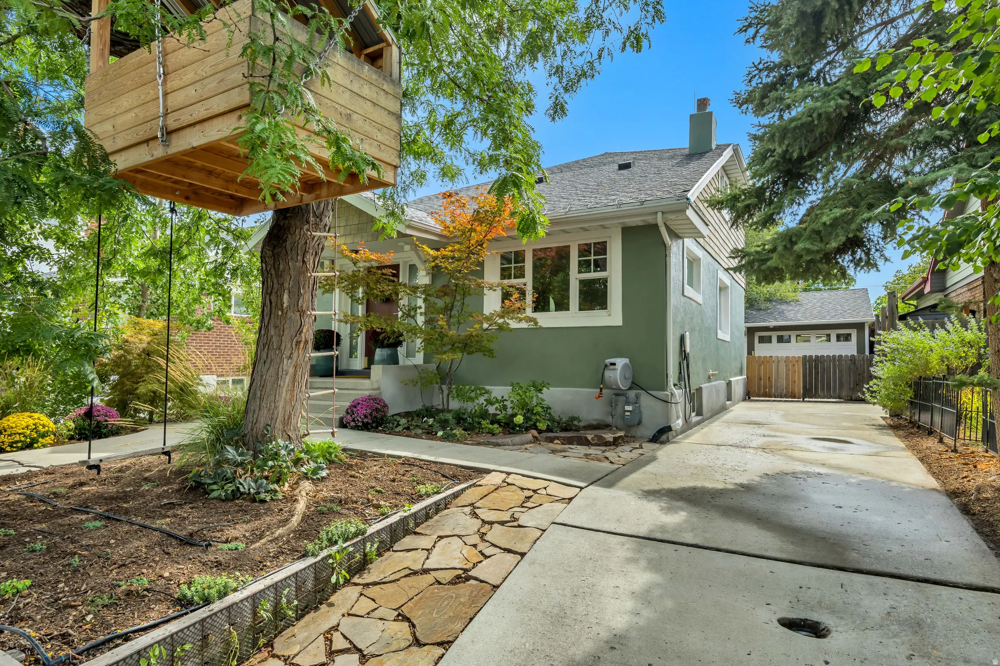 Treehouse structure with ladder, concrete driveway, stone pathway, and mature landscaping