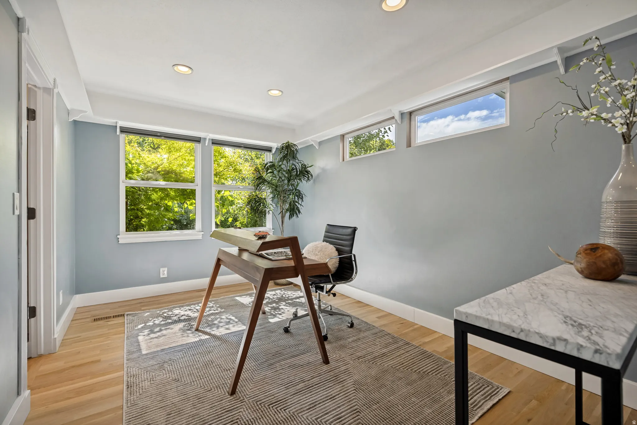 Recessed ceiling lighting, wood-finish flooring, multiple windows, and a built-in desk with a stone-finish countertop