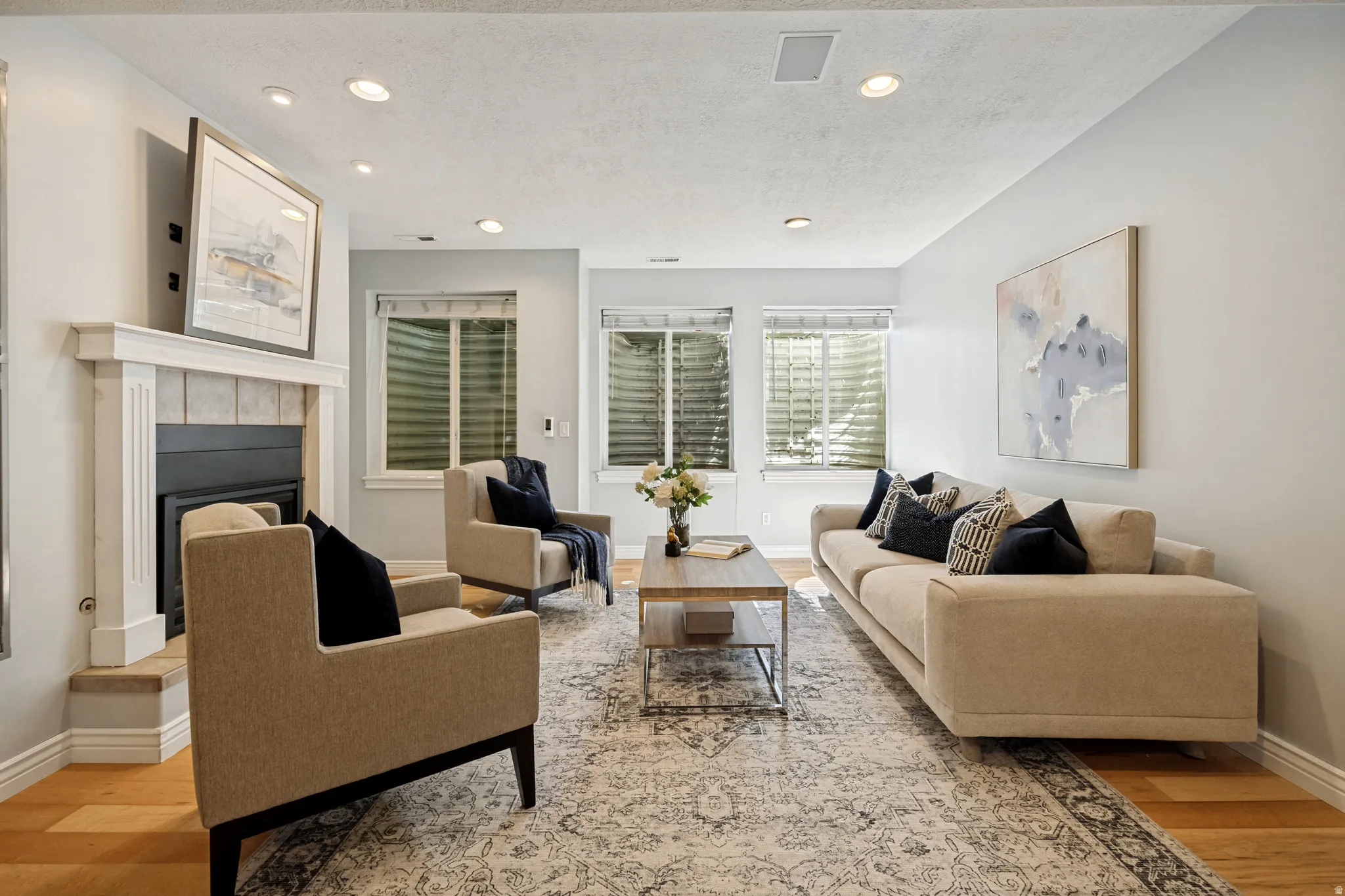 Living area featuring wood flooring, a fireplace with a white mantel, recessed lighting, and multiple windows
